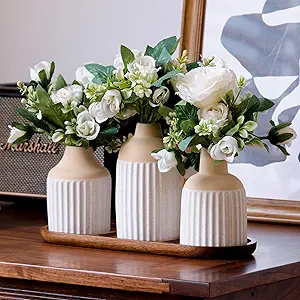 Set of three ceramic vases with white artificial flowers and greenery on a wooden tray