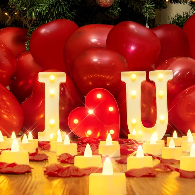 Romantic setup with "I ❤️ U" light-up letters, surrounded by red heart-shaped balloons, rose petals, and candles.