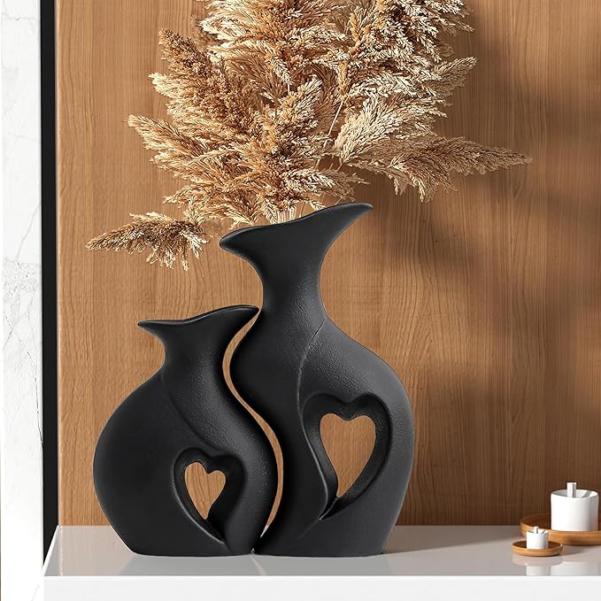 Modern black ceramic vases with heart-shaped cutouts and dried pampas grass on a white shelf