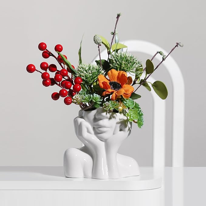 Modern ceramic face vase with colorful artificial flowers and berries on a white table